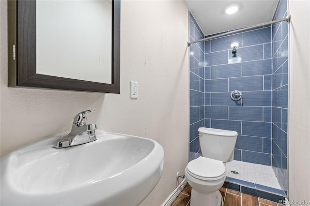 bathroom with wood-type flooring, tiled shower, sink, and toilet