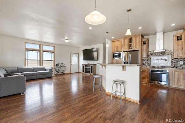 kitchen featuring appliances with stainless steel finishes, dark wood-type flooring, wall chimney range hood, and a breakfast bar