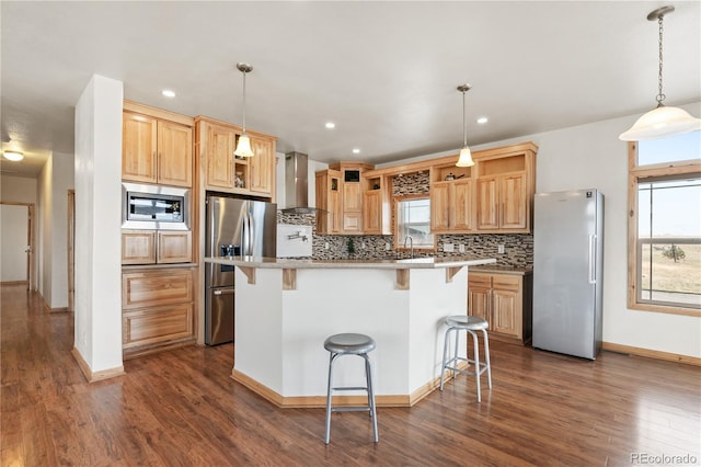 kitchen featuring stainless steel appliances, wall chimney exhaust hood, a kitchen breakfast bar, and a wealth of natural light