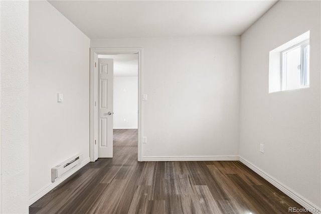 unfurnished room featuring baseboard heating and dark hardwood / wood-style flooring