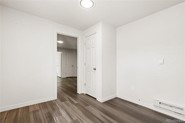 unfurnished room featuring a baseboard heating unit and dark hardwood / wood-style flooring