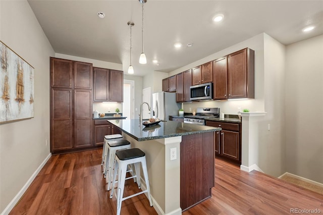 kitchen featuring dark wood-style flooring, appliances with stainless steel finishes, an island with sink, and a breakfast bar area