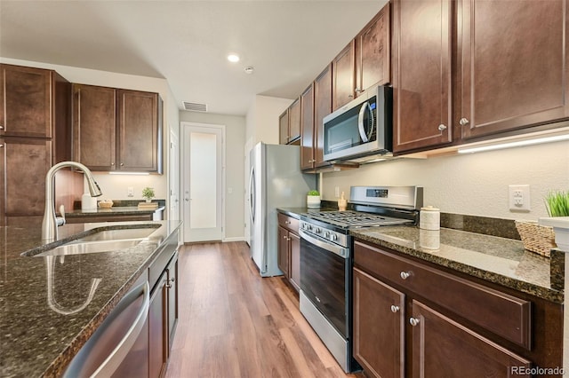 kitchen with appliances with stainless steel finishes, dark stone counters, light wood-type flooring, and a sink