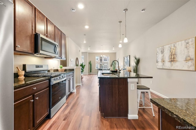 kitchen with a breakfast bar area, stainless steel appliances, hanging light fixtures, a kitchen island with sink, and a sink