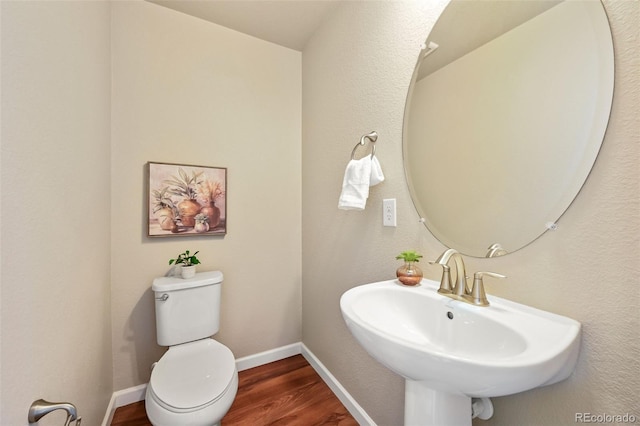 half bath with wood finished floors, a sink, toilet, and baseboards