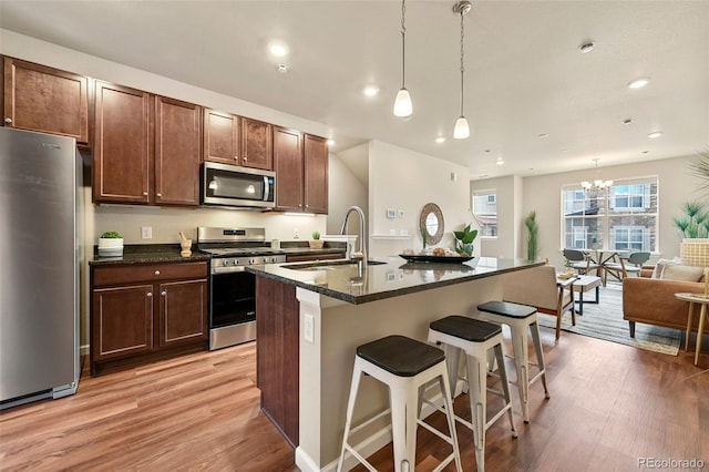 kitchen featuring decorative light fixtures, a center island with sink, stainless steel appliances, light wood-style flooring, and open floor plan