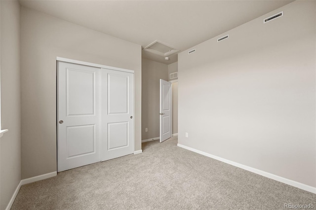 unfurnished bedroom featuring attic access, a closet, light colored carpet, and baseboards