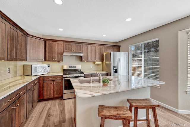 kitchen with under cabinet range hood, backsplash, appliances with stainless steel finishes, and a sink