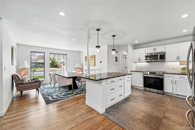 kitchen featuring appliances with stainless steel finishes, wood finished floors, tasteful backsplash, white cabinets, and a center island