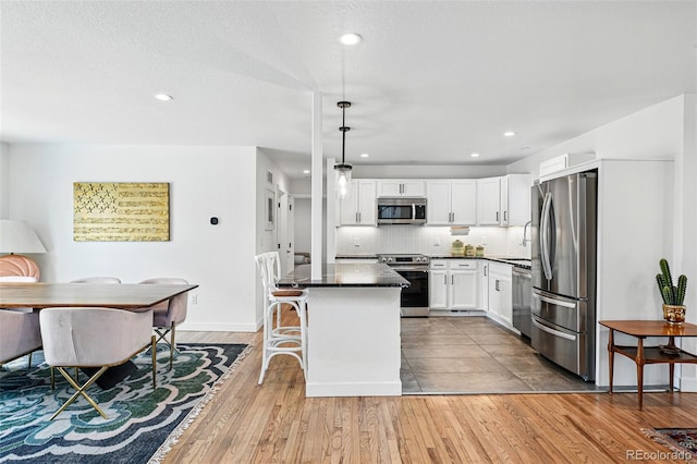 kitchen featuring appliances with stainless steel finishes, dark countertops, white cabinets, wood finished floors, and decorative backsplash