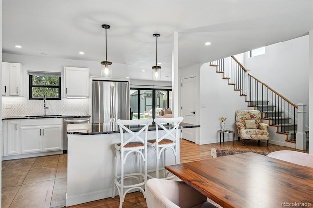kitchen with stainless steel appliances, a sink, dark countertops, decorative backsplash, and white cabinetry