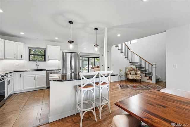 kitchen featuring stainless steel appliances, a sink, a breakfast bar, dark countertops, and recessed lighting