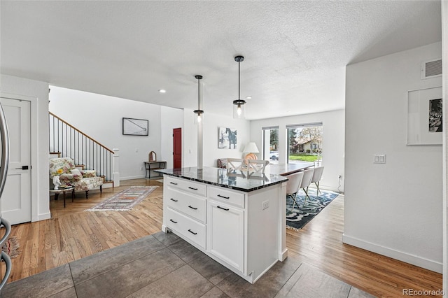 kitchen featuring white cabinets, open floor plan, a center island, pendant lighting, and light wood-style flooring