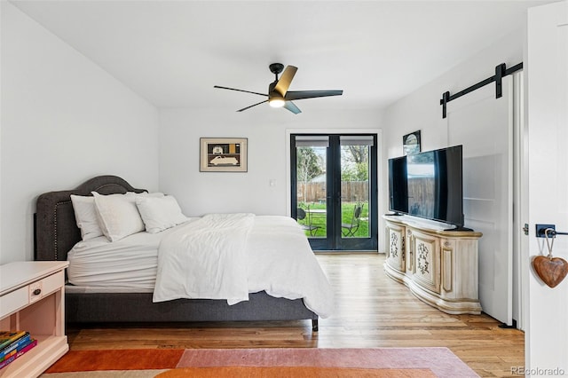 bedroom featuring light wood-type flooring, access to outside, a barn door, a ceiling fan, and french doors