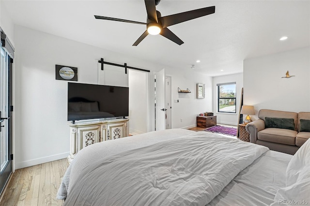 bedroom featuring a barn door, light wood finished floors, baseboards, recessed lighting, and a ceiling fan