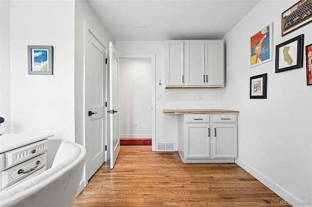 kitchen featuring light wood finished floors, baseboards, light countertops, and white cabinets