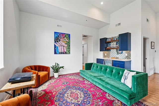 living area featuring wet bar, baseboards, a high ceiling, wine cooler, and light wood finished floors