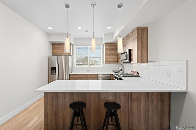 kitchen with a kitchen bar, hanging light fixtures, appliances with stainless steel finishes, kitchen peninsula, and decorative backsplash