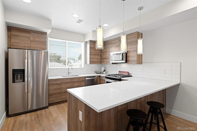 kitchen with pendant lighting, stainless steel appliances, kitchen peninsula, and sink