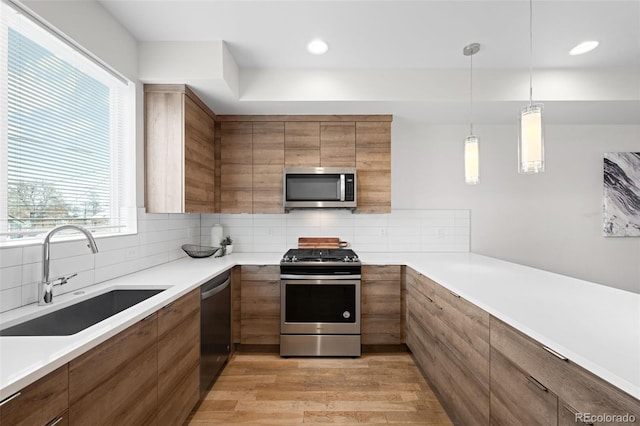 kitchen with sink, appliances with stainless steel finishes, backsplash, light hardwood / wood-style floors, and decorative light fixtures