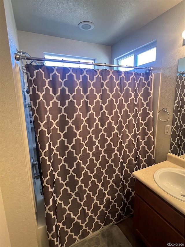 bathroom with vanity, shower / tub combo with curtain, and a textured ceiling