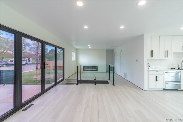 unfurnished living room featuring light wood-style floors, recessed lighting, visible vents, and a sink