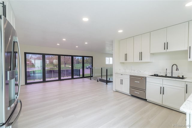 kitchen featuring stainless steel appliances, white cabinetry, a sink, and light wood-style flooring