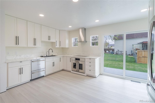 kitchen with black electric stovetop, a sink, stainless steel oven, white cabinets, and wall chimney exhaust hood