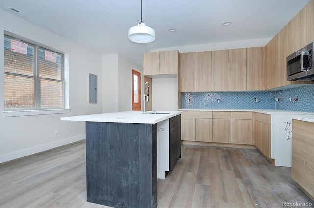 kitchen featuring pendant lighting, light brown cabinets, a kitchen island with sink, light hardwood / wood-style flooring, and decorative backsplash