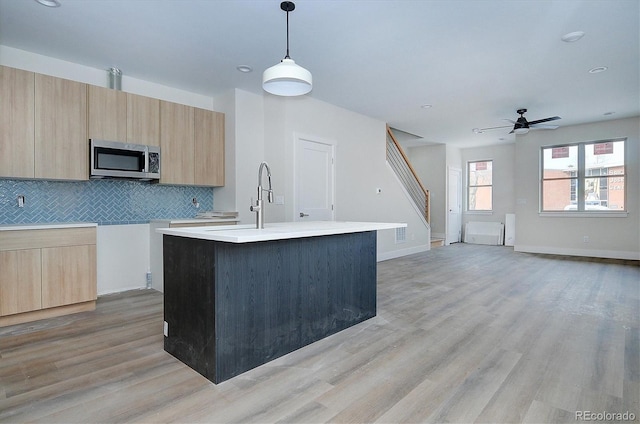 kitchen featuring light brown cabinets, decorative light fixtures, a kitchen island with sink, and ceiling fan