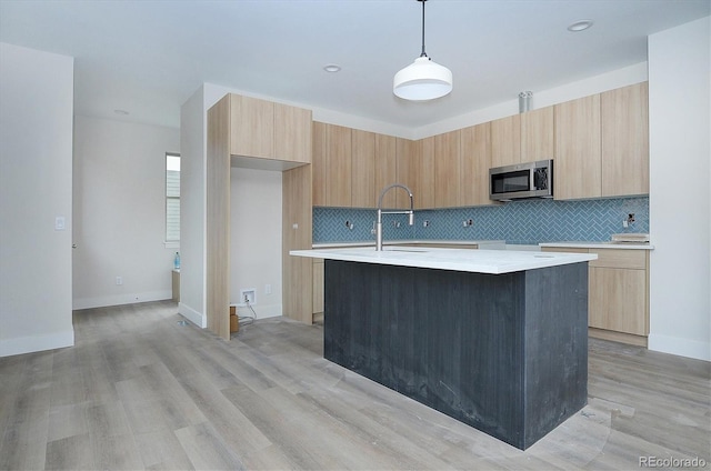 kitchen with decorative backsplash, light brown cabinets, light hardwood / wood-style floors, hanging light fixtures, and an island with sink