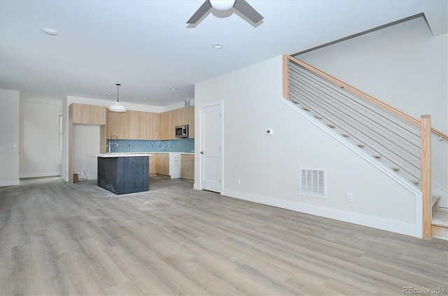 kitchen with backsplash, ceiling fan, light hardwood / wood-style floors, decorative light fixtures, and a kitchen island