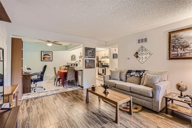 living room featuring a textured ceiling, baseboards, visible vents, and a ceiling fan