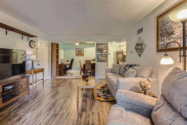 living room featuring a textured ceiling, ceiling fan, wood finished floors, visible vents, and baseboards