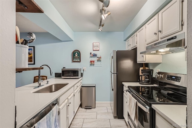 kitchen featuring under cabinet range hood, a sink, light countertops, appliances with stainless steel finishes, and rail lighting