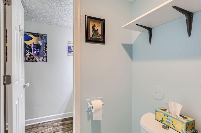 bathroom with toilet, a textured ceiling, baseboards, and wood finished floors