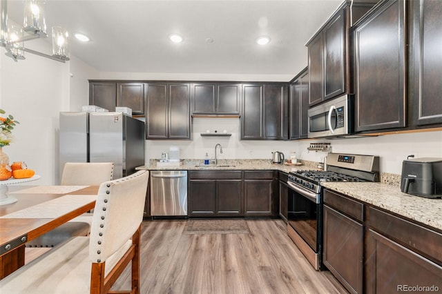 kitchen with light stone countertops, appliances with stainless steel finishes, sink, light hardwood / wood-style flooring, and pendant lighting