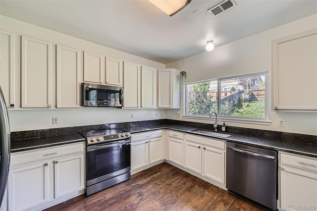 kitchen featuring stainless steel appliances, dark hardwood / wood-style flooring, white cabinetry, sink, and dark stone counters