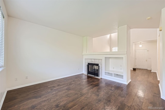 unfurnished living room featuring built in features, a tile fireplace, and dark hardwood / wood-style flooring