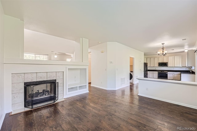 unfurnished living room with a tiled fireplace, dark hardwood / wood-style floors, a notable chandelier, washer / dryer, and sink