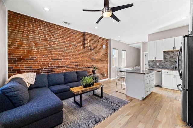 living room with ceiling fan, light wood-style flooring, brick wall, visible vents, and baseboards