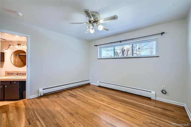 unfurnished bedroom featuring baseboard heating, ensuite bath, sink, and light hardwood / wood-style flooring