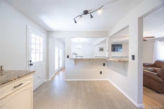 kitchen featuring light hardwood / wood-style flooring, a kitchen breakfast bar, an inviting chandelier, and light stone countertops