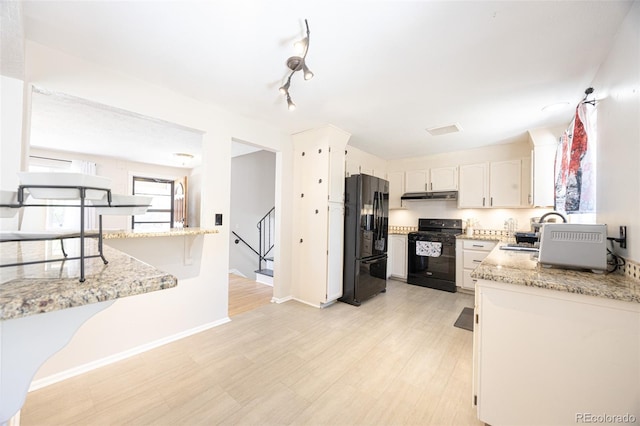 kitchen with black appliances, light hardwood / wood-style floors, light stone countertops, and white cabinets