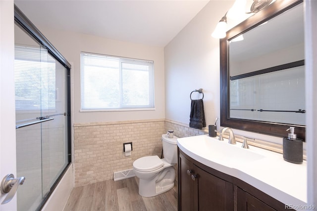 full bathroom featuring tile walls, hardwood / wood-style floors, bath / shower combo with glass door, vanity, and toilet