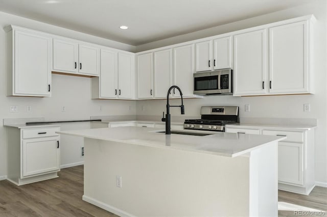 kitchen featuring a center island with sink, white cabinets, sink, light wood-type flooring, and stainless steel appliances