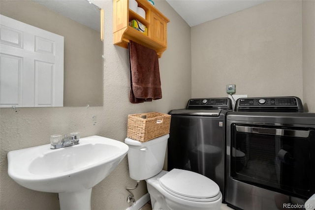 bathroom with sink, washing machine and clothes dryer, and toilet