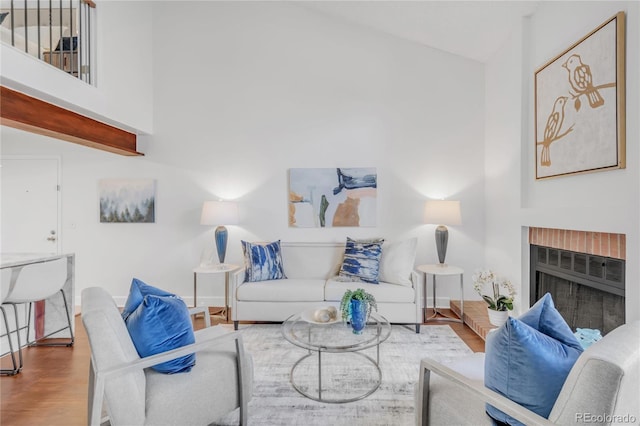 living area with a towering ceiling, a brick fireplace, baseboards, and wood finished floors