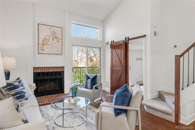 living room with high vaulted ceiling, a barn door, wood finished floors, visible vents, and stairs