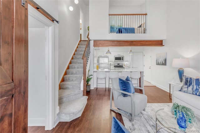 living area featuring dark wood-style floors, stairs, baseboards, and a barn door